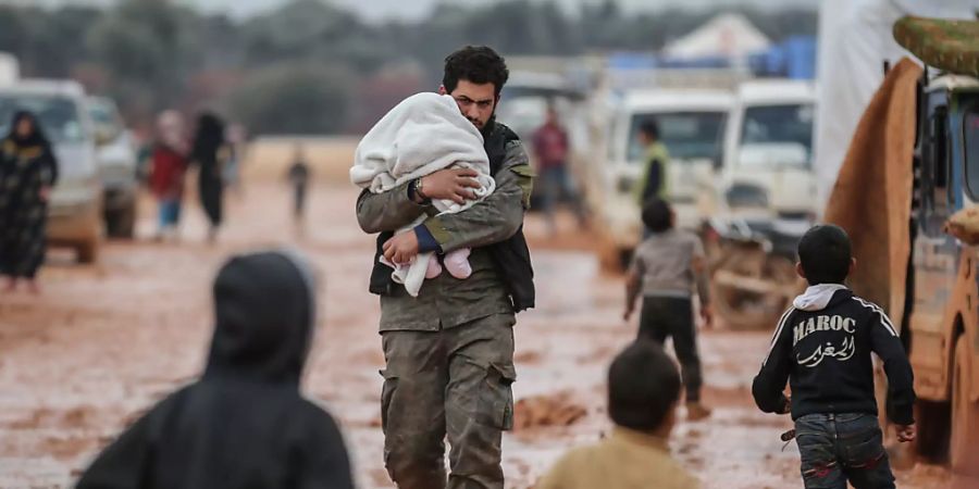 ARCHIV - Ein Syrer trägt sein Baby in einem Behelfslager für Familien, die aus Idlib vertrieben wurden. Foto: Anas Alkharboutli/dpa