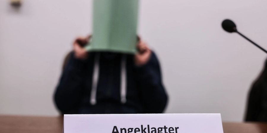 Der Angeklagte im Missbrauchskomplex Wermelskirchen hält sich im Gerichtssaal eine Mappe vor das Gesicht.