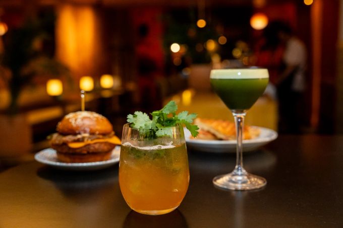 Quitten-Cocktail (orange) und Palmen-Sauer-Cocktail (grün), serviert mit einem gegrillten Käsesandwich und einem rauchigen Cheeseburger mit karamellisierten Zwiebeln. DAR Restaurant Cocktailbar