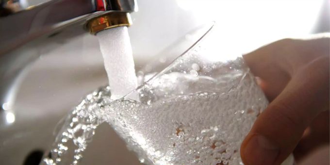 Ein Mann hält ein Glas unter einen laufenden Wasserhahn. (Symbolbild) Glas
