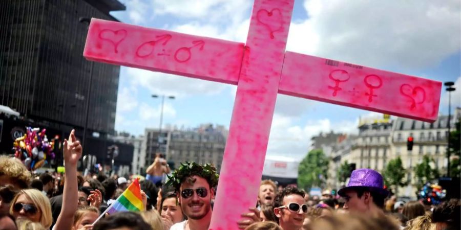 Ein Demonstrant hält ein pinkes Kreuz hoch bei der Pride Parade in Paris.