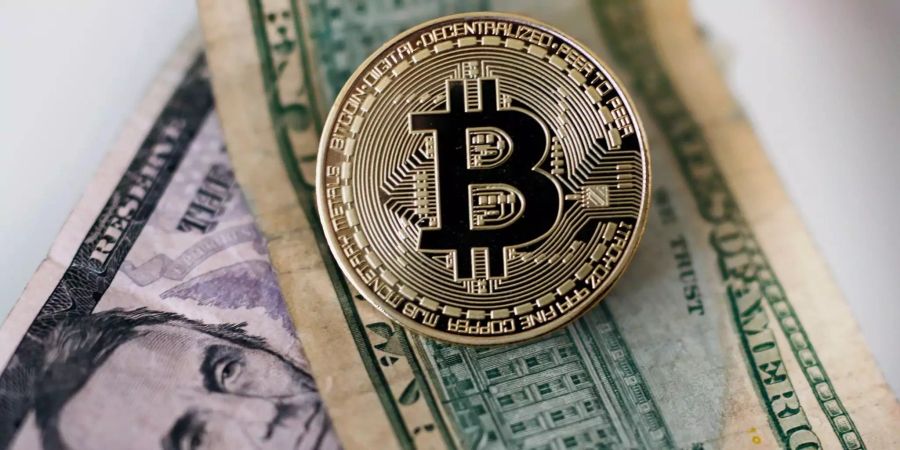 Eine Bitcoin Münze liegt auf Dollar Geldscheinen,