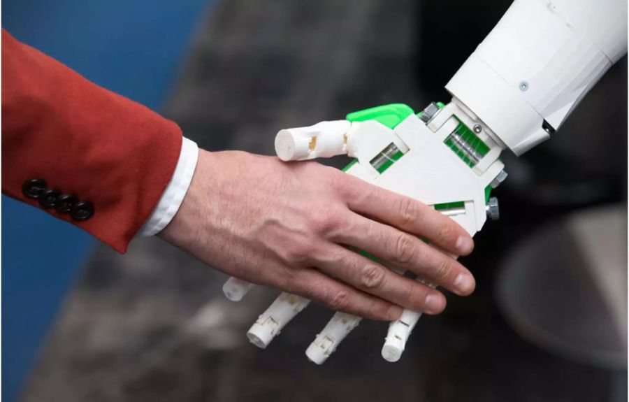 Menschliche Hand und Roboterhand geben sich einen Handschlag - Keystone