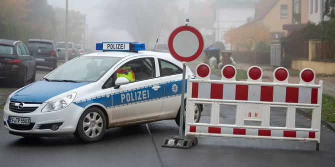 Ein Einsatzfahrzeug der Polizei steht neben einer Strassensperre.