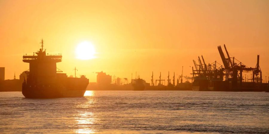 Die Sonne geht am über dem Hafen und einem Containerschiff in Hamburg auf.