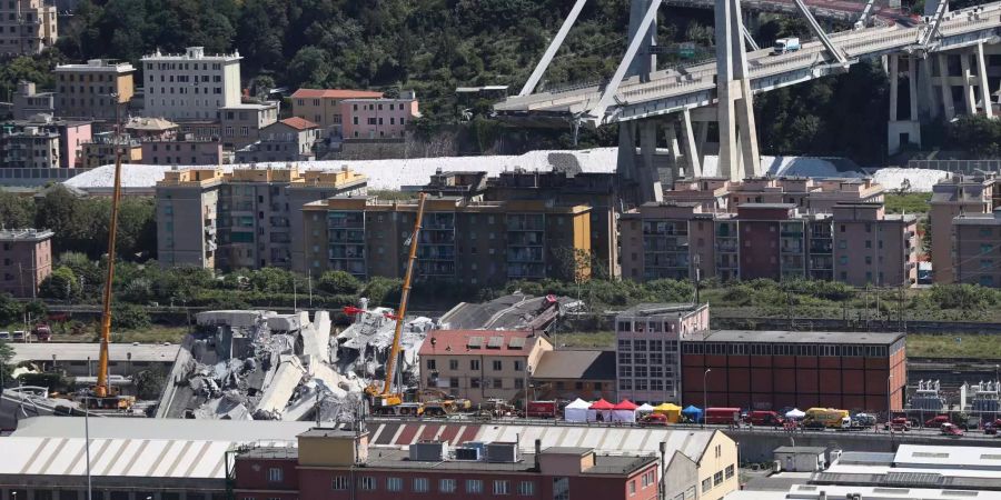 Mit Baggern und Kränen werden Trümmerteile der teilweise eingestürzten Brücke in Genua (IT) weggeräumt.