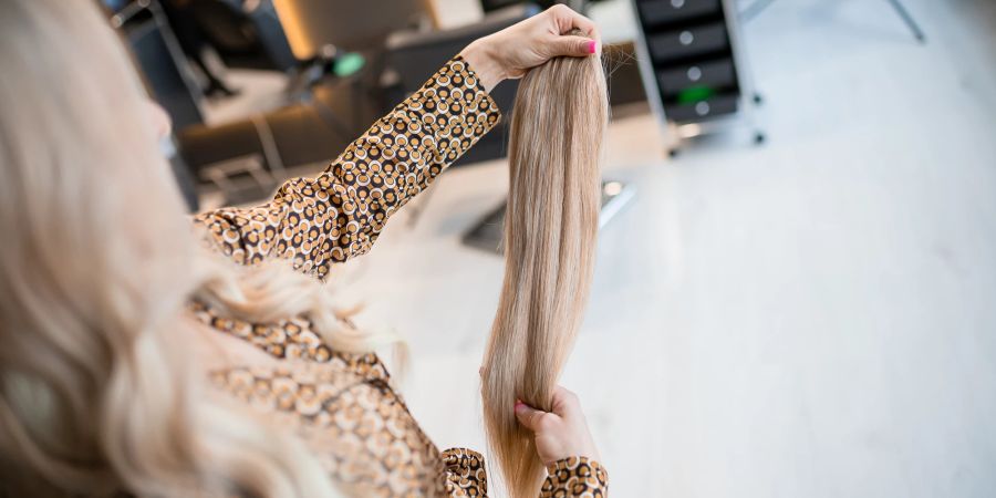 Frau betrachtet blonde Extension Strähne im Salon.