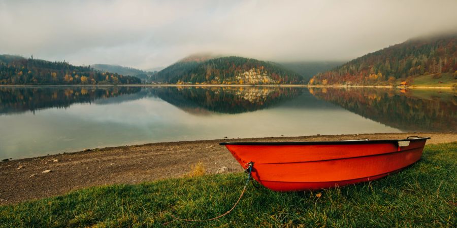 rotes boot liegt am ufer eines flusses, waldlandschaft im hintergrund