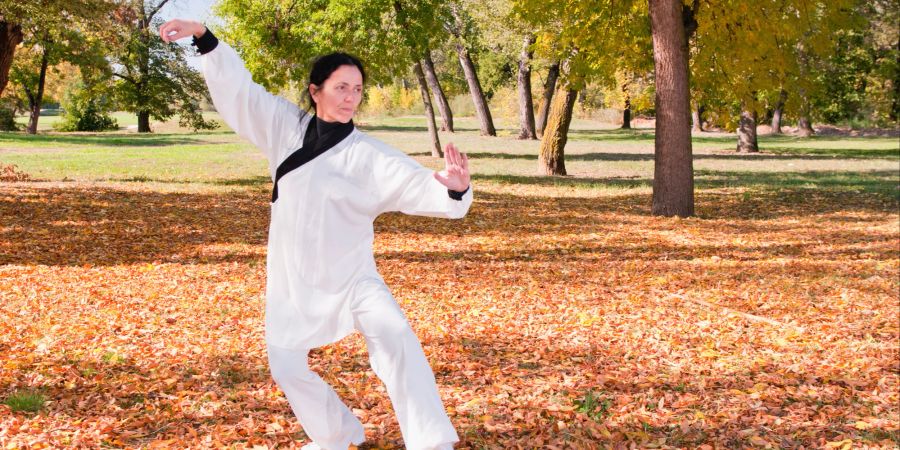 Frau im weissen Anzug macht Übungen im Wald.