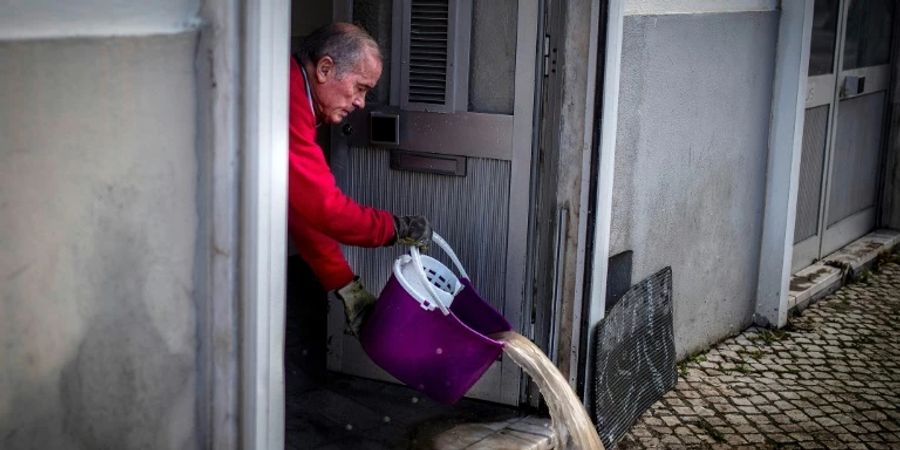 Ein Mann schüttet Wasser aus seinem Geschäft in Lissabon