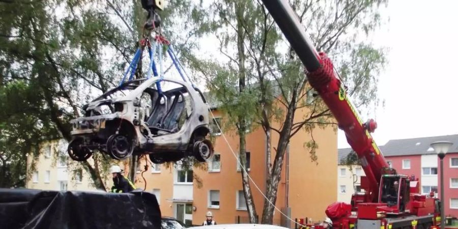 Ein Kranwagen der Dortmunder Feuerwehr hebt ein ausgebranntes E-Auto in einen Container. Foto: -/Feuerwehr Dortmund/dpa