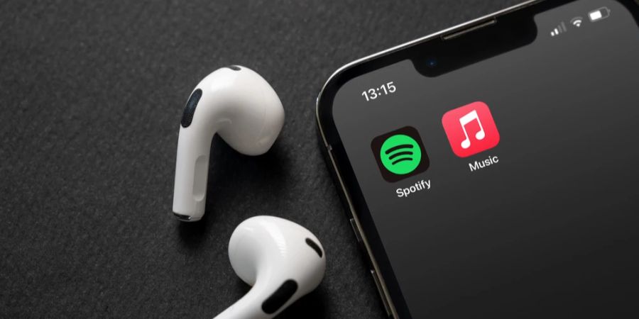 Kopfhörer kabellos neben einem Smartphone mit den beiden Apps Apple Music und Spotify auf dem Bildschirm