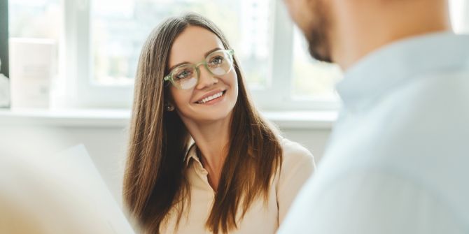 Frau mit Brille lächelt Kollegen an