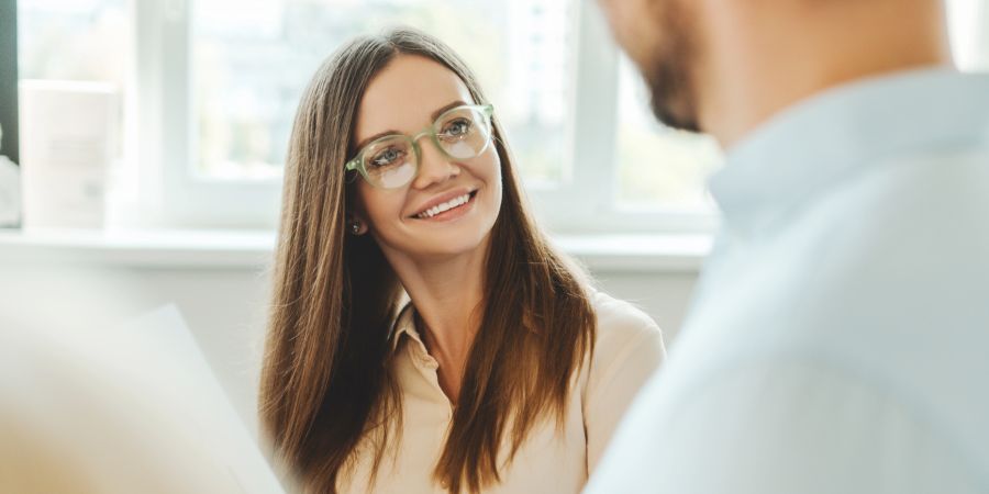 Frau mit Brille lächelt Kollegen an