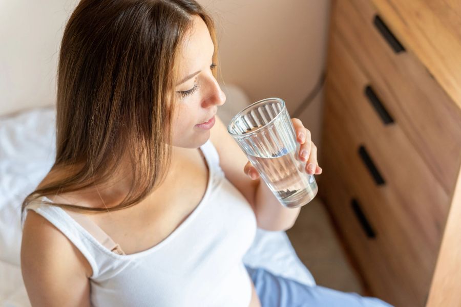 Frau trinkt Wasser im Bett.