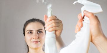 Frau putzt Spiegel mit Wasserflasche