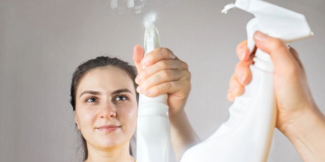 Frau putzt Spiegel mit Wasserflasche
