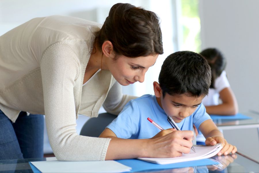 Lehrerin und Schüler schreiben auf einem Heft