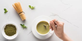 Geschnittene Ansicht einer Frau mit Matcha-Matcha-Tee auf dem Tisch mit Schneebesen, Pulver und Minze