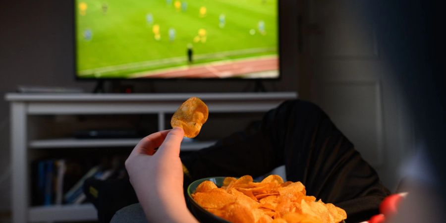 Ein Junge sitzt vor dem Fernseher und ist dabei Kartoffelchips.