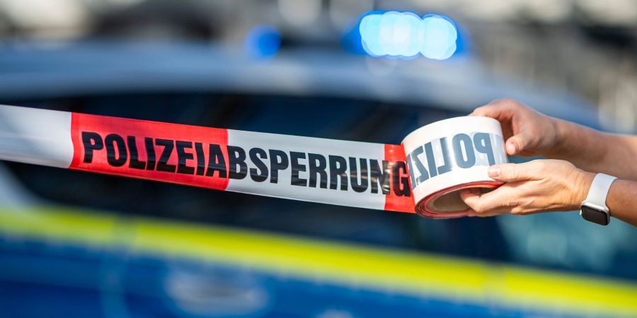 Ein Absperrband wird vor einem Polizeiwagen ausgerollt. (Archivbild)
