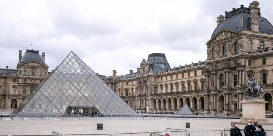 Der Louvre ist geschlossen, der Platz davor ist leer. Nur drei Polizisten gehen an einer Absperrung entlang. Foto: Elko Hirsch/dpa