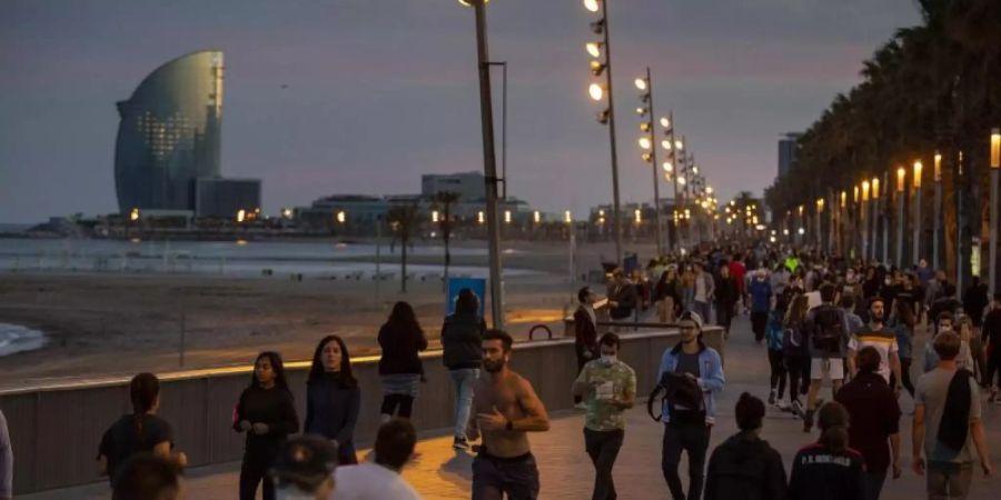Menschen gehen bei Sonnenuntergang auf einer Strandpromenade spazieren und treiben Sport. Foto: Emilio Morenatti/AP/dpa