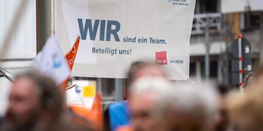 "Wir sind ein Team. Beteiligt uns!" steht auf einem Plakat, das während eines Warnstreiks von Mitarbeitern des WDR aufgehängt wurde. Foto: Marius Becker