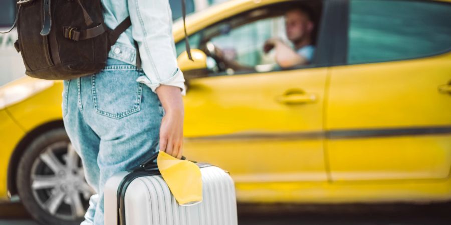 Frau mit Koffer in der Hand will in ein gelbes Taxi steigen.