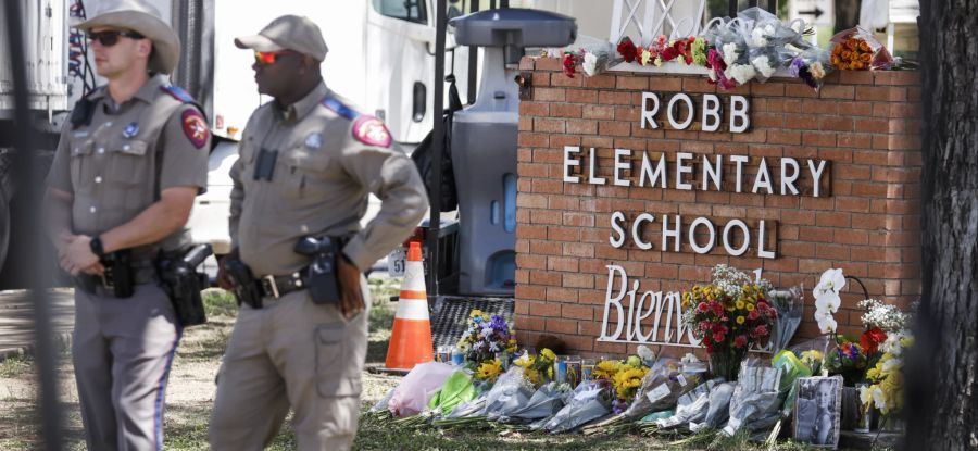 Beamte der Texas Highway Patrol stehen am Tatort des Massakers in der Robb Elementary School in Uvalde, Texas, neben einem Blumengebinde.