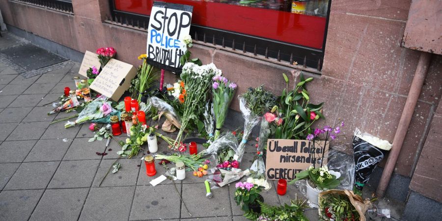 Blumen, Kerzen und Schilder liegen an dem Ort, an dem am Montag (02.05.2022) ein Mann nach einer Polizeikontrolle in Mannheim gestorben ist.