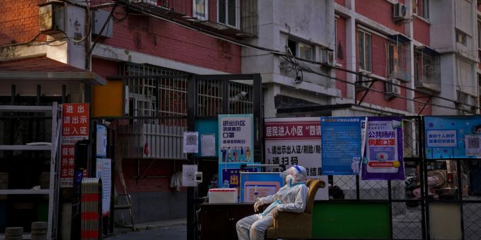 Ein Wachmann im Schutzanzug sitzt an einem Eingangstor zu einem Wohnviertel in Peking. corona china