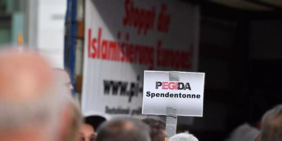 Auf einer Kundgebung von Pegida halten Anhänger ein Schild mit dem Schriftzug «Pegida Spendentonne» in die Höhe. Foto: Zentralbild/dpa-Zentralbild/dpa