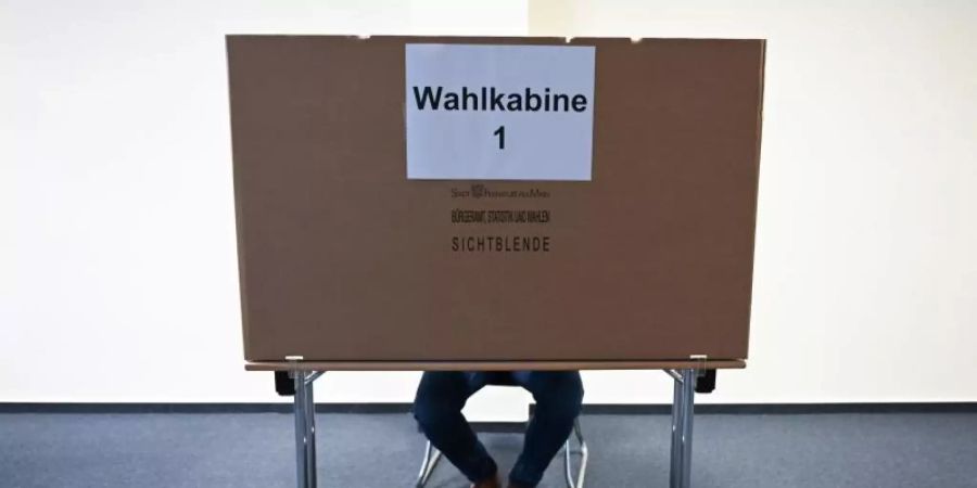 Ein Mann sitzt im Wahlraum des Briefwahllokals Frankfurt Innenstadt hinter einer Wahlkabine. Foto: Arne Dedert/dpa