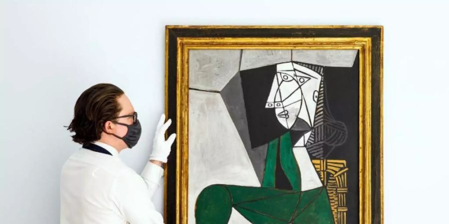 Ein Mitarbeiter von Sotheby's hängt das Gemälde «Femme assise en costume» von Pablo Picasso (gemalt 1953) auf. Foto: ---/Sotheby’s/dpa