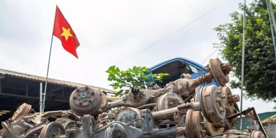 Die Flagge Vietnams weht in Te Lo über einem Haufen rostiger Autoachsen, dahinter steht eine leere LKW-Kabine. Foto: Chris Humphrey/dpa