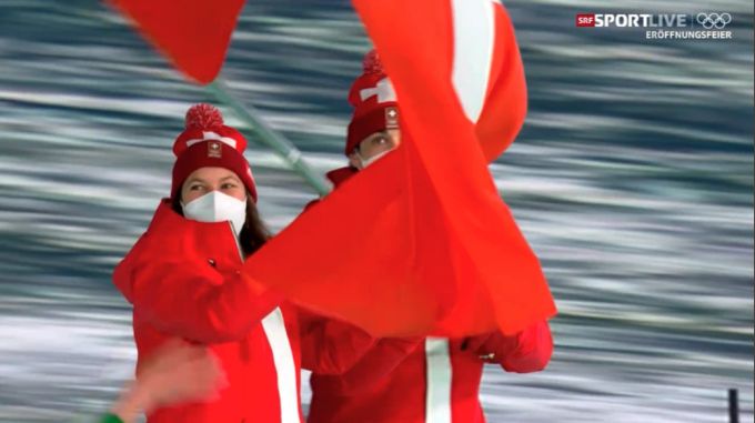 Wendy Holdener strahlt hinter der Maske, neben ihr marschiert Andres Ambühl. olympia 2022