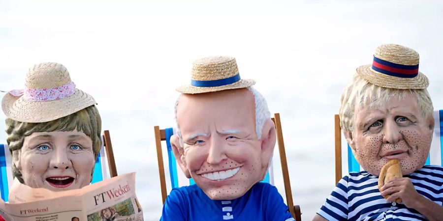 Klimaaktivisten von Oxfam, die riesige Köpfe tragen, die die Staats- und Regierungschefs der G7 (l-r) Bundeskanzlerin Angela Merkel, US-Präsident Joe Biden, der britische Premierminister Boris Johnson darstellen sollen, sitzen auf Strandliegen, während sie an einer Aktion am Swanpool Beach teilnehmen. Foto: Alastair Grant/AP/dpa