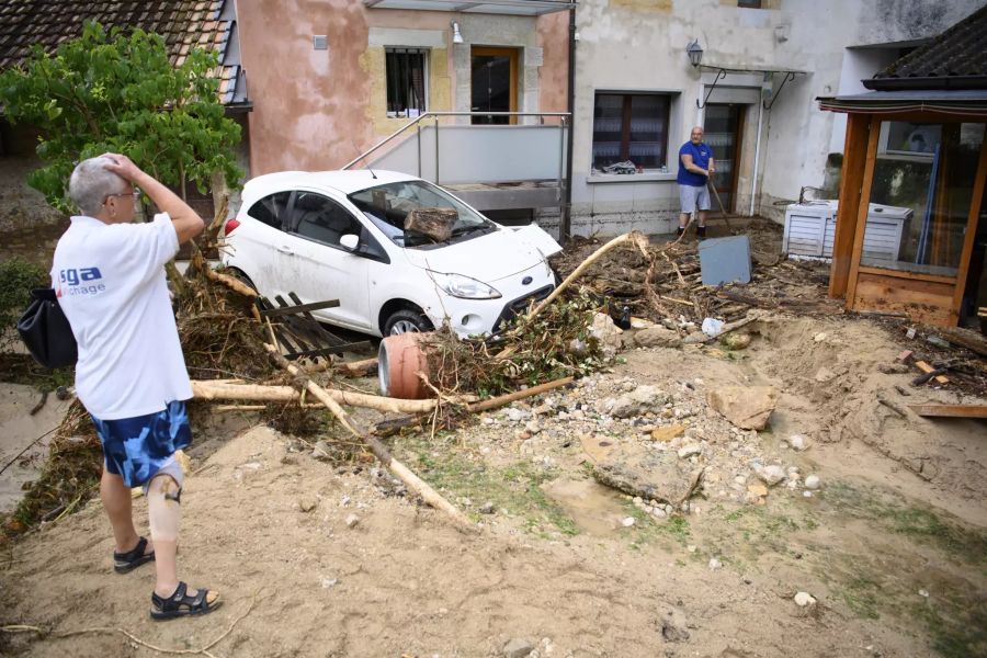 Eine Person betrachtet die Schäden und ein Autowrack nach einem heftigen Sturm.