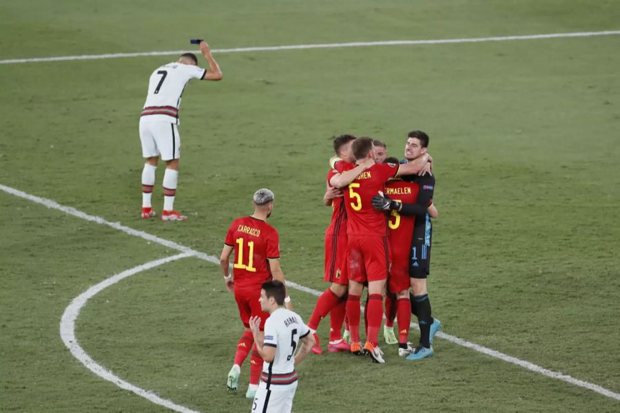 Die Belgier freuen sich über den Viertelfinal-Einzug an der Euro 2020. Im Hintergrund ist Cristiano Ronaldo zu sehen, wie er die Captain-Binde zu Boden wirft.