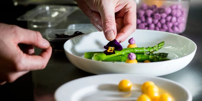 Fein und schön anzusehen: Tim Raues Gericht mit grünem Spargel bekommt am Ende eine Veilchen-Dekoration. Teller Uchuva Hand Spargel Gericht