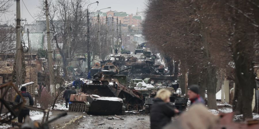 Zivilisten laufen am 1. März 2022 durch eine Strasse in Bucha, nahe Kiew, in der zerstörte russische Militärfahrzeuge stehen.