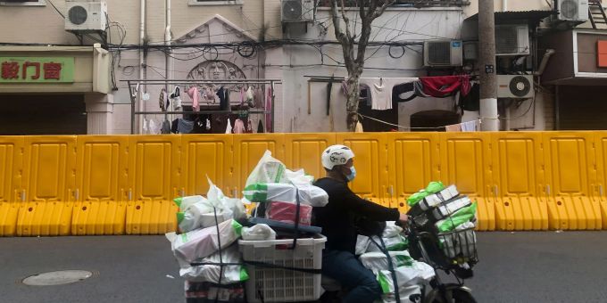 Ein Lieferservice fährt an den Absperrungen vorbei, die errichtet wurden, um eine Gemeinde in Shanghai abzuriegeln. Shanghai
