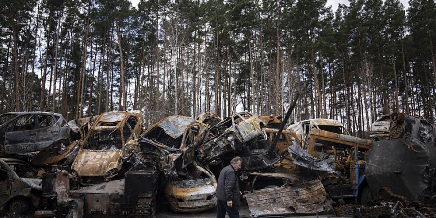 Ein Mann geht in einem Aussenbezirk von Kiew an einem Lagerplatz für verbrannte bewaffnete Fahrzeuge und Autos vorbei. Foto: Evgeniy Maloletka/AP/dpa