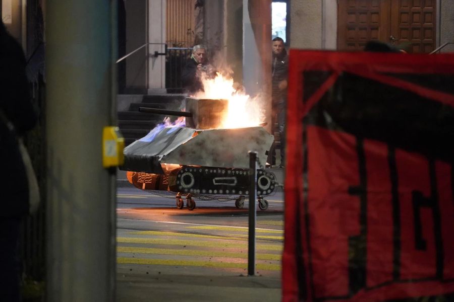 Ausserdem verbrennen Demonstrierende einen selbstgebastelten Panzer auf der Strasse und lassen die Reste zurück.