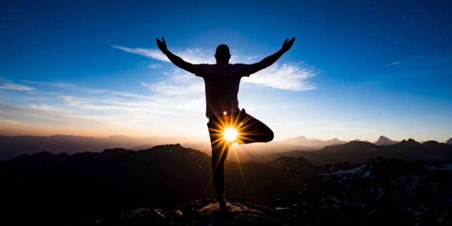 Ein Mann macht Yoga beim Sonnenaufgang.