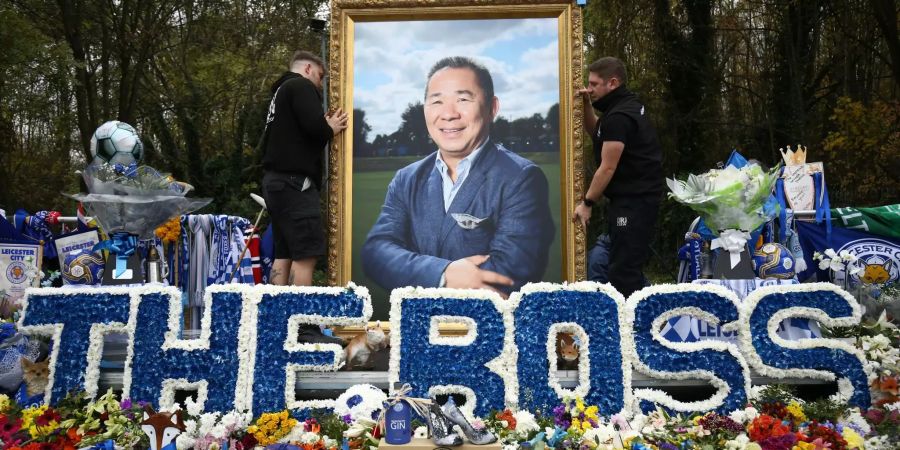 Freiwillige richten ein Porträt von Leicester Präsident Srivaddhanaprabha aus, im Vordergrund liegen Blumen und Fanartikel des Vereins.