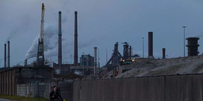 Ein Radfahrer fährt an einem Industriegelände vorbei.