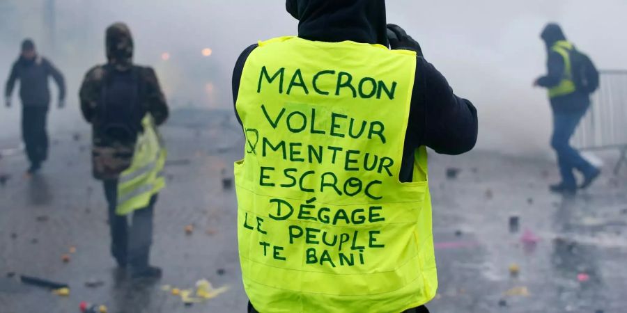 : Ein Demonstrant trägt eine Warnweste auf der zu lesen ist «Macron, Dieb, Lügner, Gauner, verschwinde, das Volk verbannt dich».