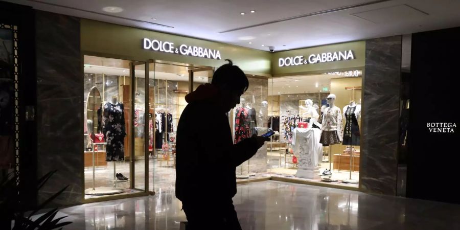 Ein Mann schaut in Peking (CHN) auf sein Natel an einem Dolce & Gabbana-Laden vorbeiläuft.